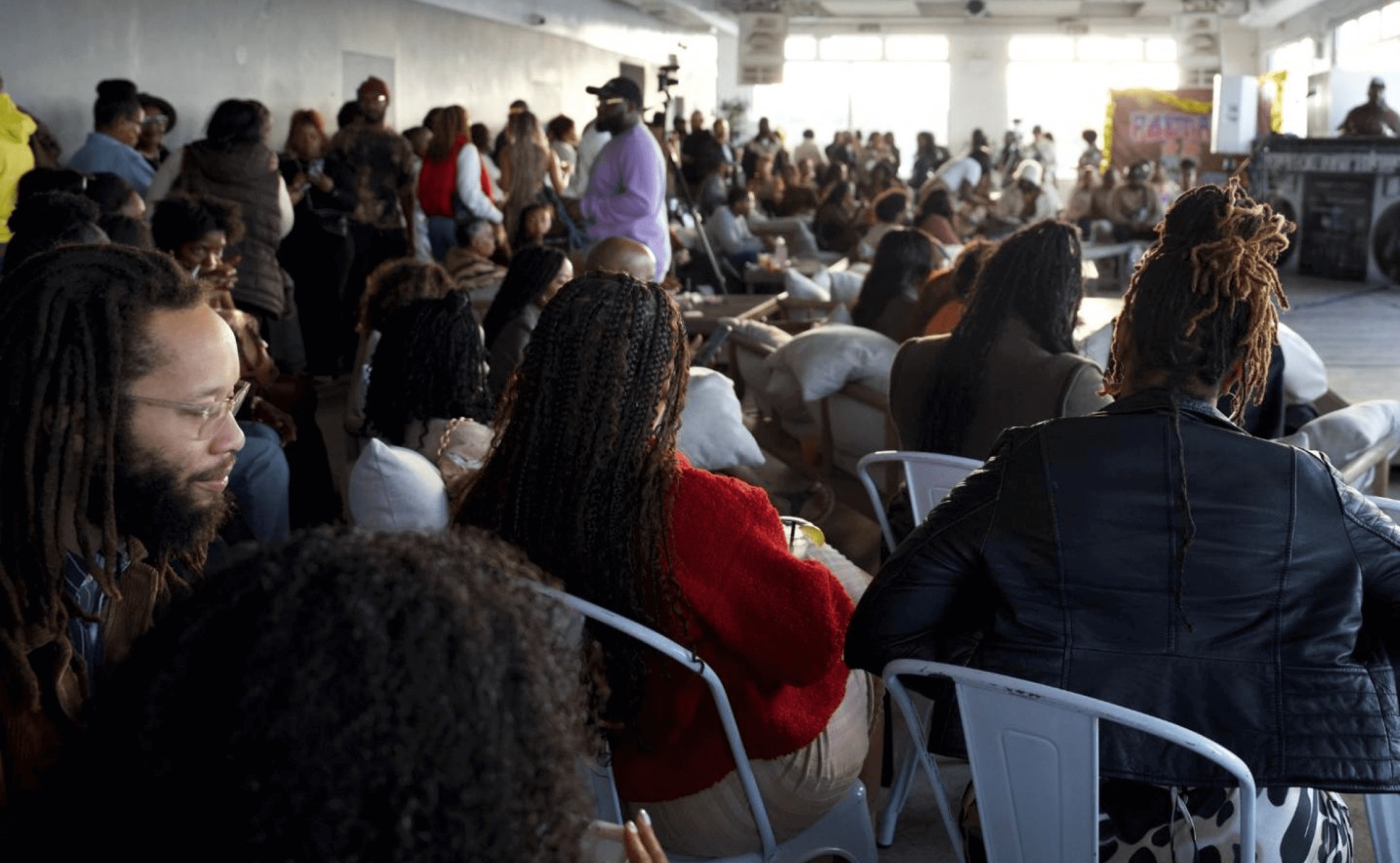 People mill about in a room whilst are seated. The space is arranged so that everyone can see wchbother as they discuss issues.
